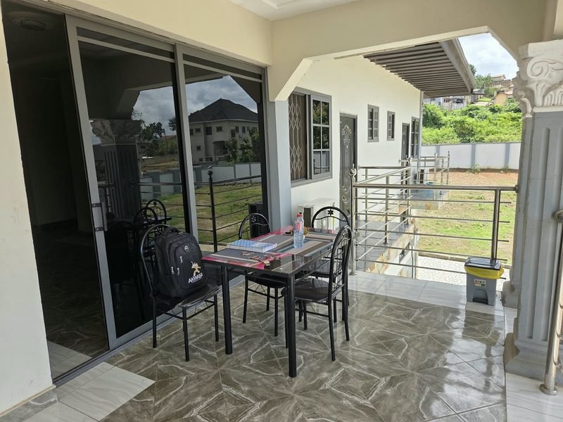 A shaded terrace with a table and chairs, looking out over the grounds